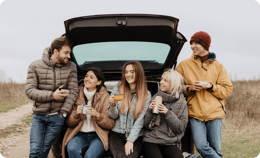 A group of friends having a day trip and relaxing next to their car.
