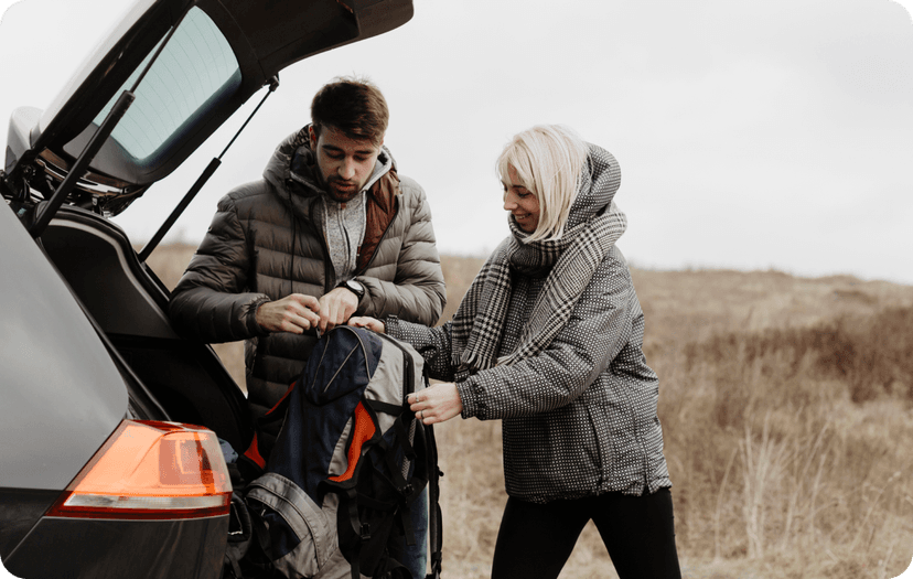 Two friends taking their backpacks out from the car.