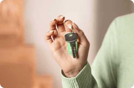 person in a green sweater holding a set of keys with stacked boxes in the background