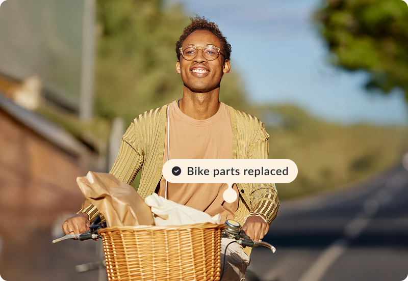 Person riding a bicycle, smiling on a sunny road. A label reads 'Bike parts replaced'.