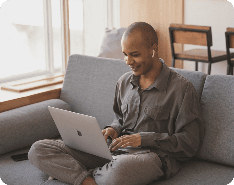 a smiling guy sitting on a sofa with his laptop on his lap