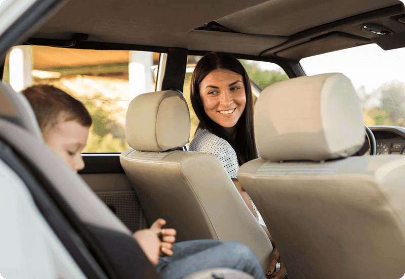 Lady looking at her child in the back seat of their car.
