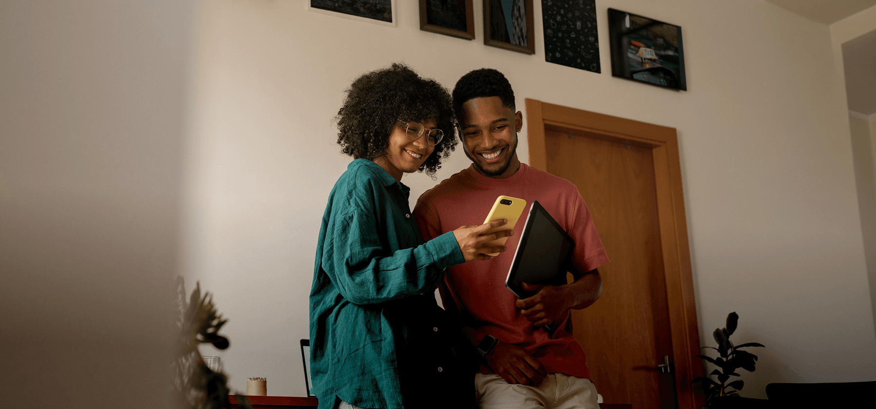 A young couple smiling and looking at a smartphone together in a home living room in France.