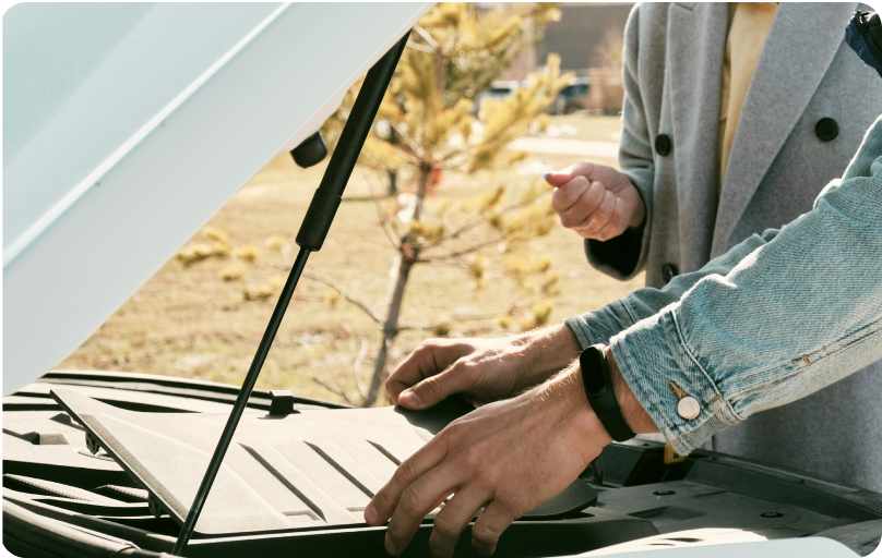 A car with opened front bonnet and two people checking a car engine.