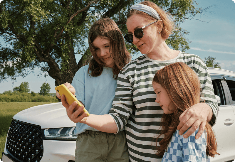 A woman and her two daughters checking her phone next to a broken car in Portugal.