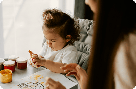 Una niña jugando con pinturas junto a su niñera.