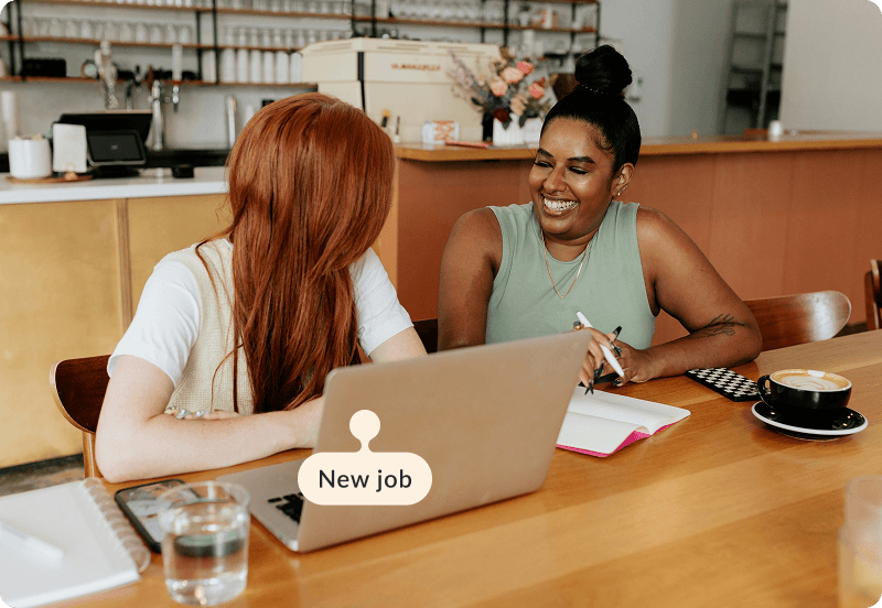Two people sitting in a cafe, working and laughing together.