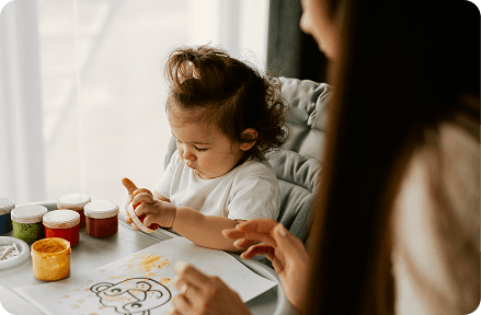 Child playing with colorful paints with her nanny.
