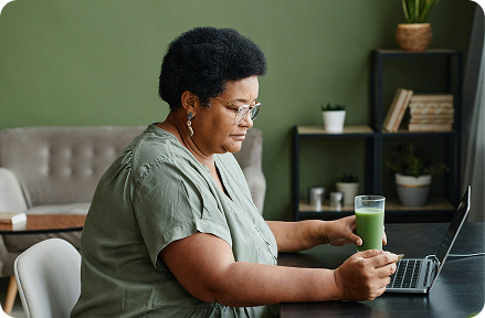 Retiree sitting in from of her laptop at home and drinking smoothie.
