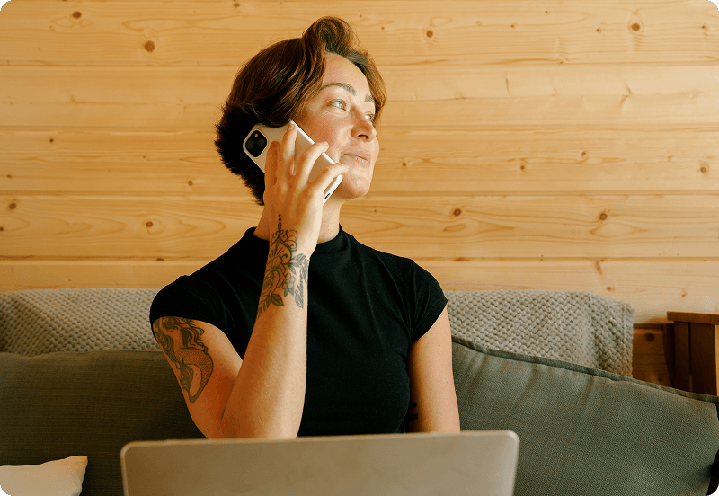 Girl talking on a phone, smiling and working on her laptop.