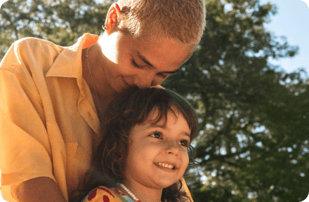 Young mother and her daughter in a park, smiling and playing on a playground.