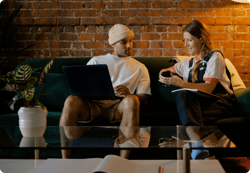 Two people sitting on a couch at the office, discussing a work project.