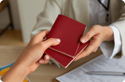 A public office representative handing over two passports to a person across the table.
