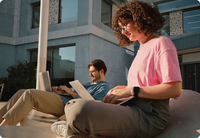 Students working on laptops in front of university buildings