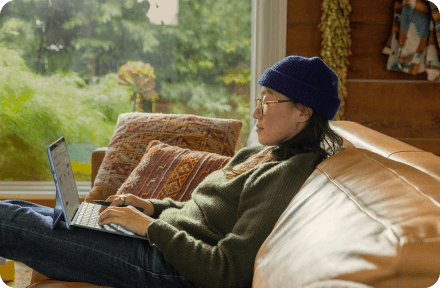 Person sitting on a couch at home, working on their computer.