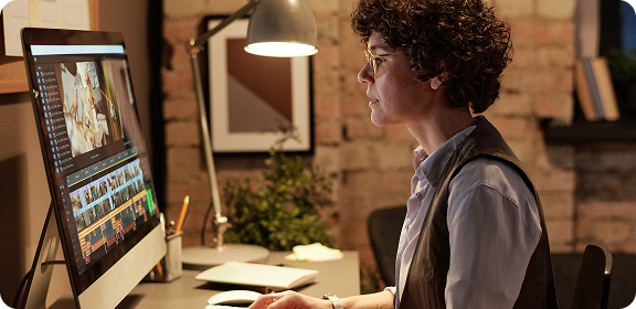 A woman working at her desk, in front of a computer screen, editing a video.
