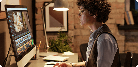 A woman working at her desk, in front of a computer screen, editing a video.