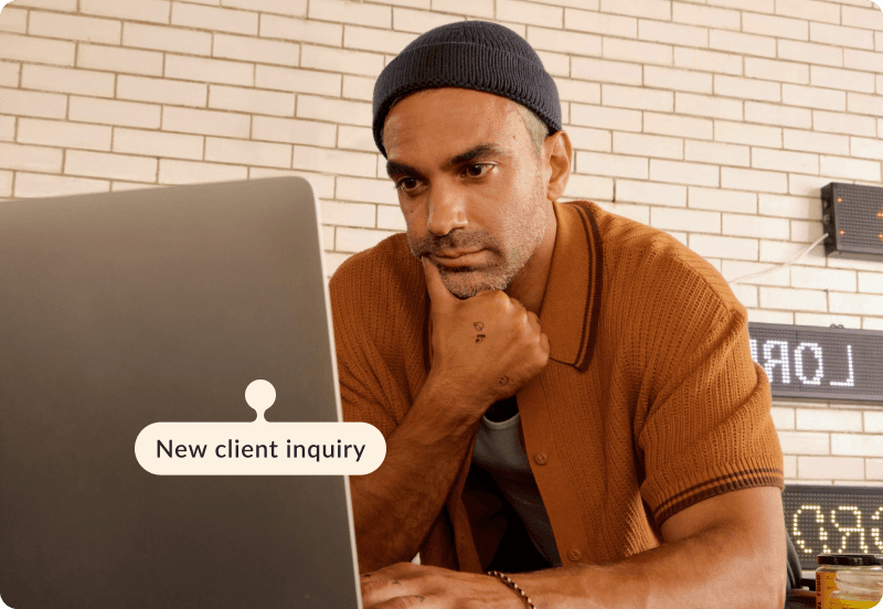 A freelancer working on his computer in a cafe. The tag reads "New client inquiry".