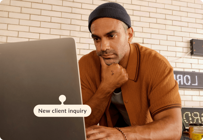 A freelancer working on his computer in a cafe. The tag reads "New client inquiry".