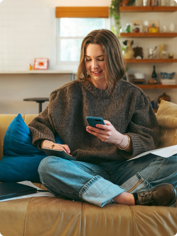 Person sitting on a couch at home, smiling and holding their phone.