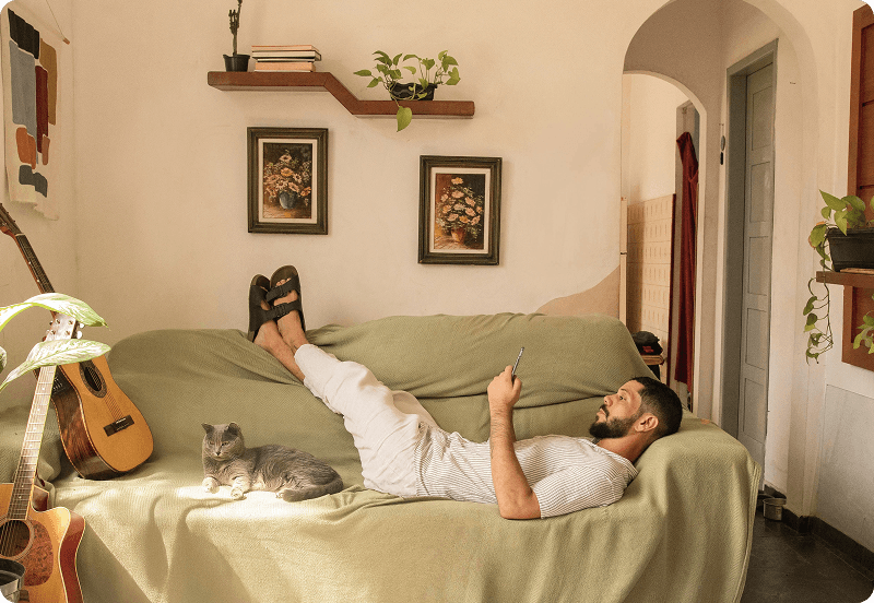 Persona acostada en un sofá en su acogedor hogar, mirando su teléfono, con un gato acostado a su lado.