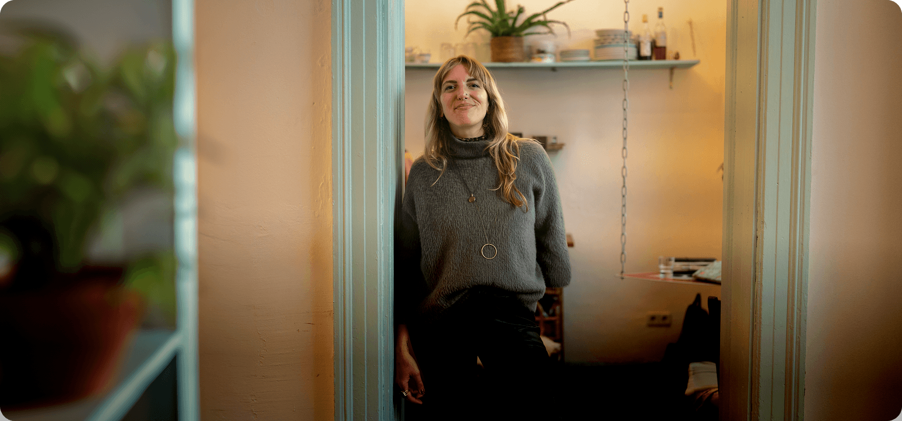 A woman with blonde hair standing in a doorway smiling in a warmly lit home interior in France.