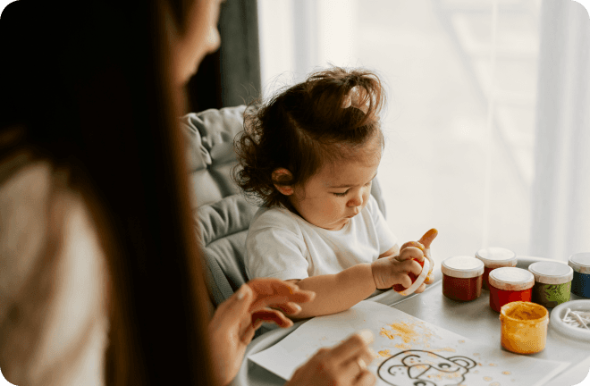 A baby playing with some paints with her mom.