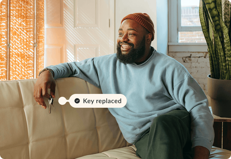 Person sitting on a couch at home, smiling and holding keys in their fingers. The tag reads "Key replaced"