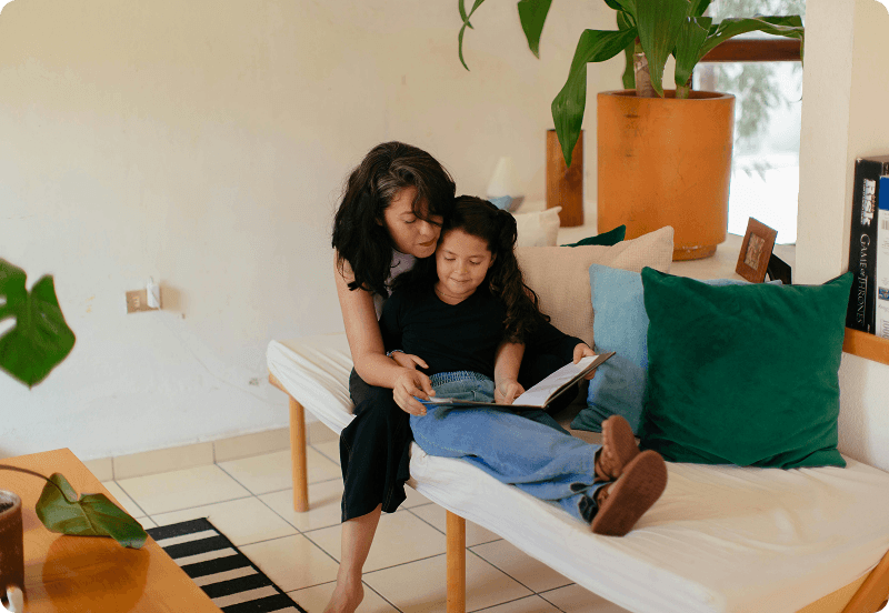 A woman sitting on a couch with her daughter, and reading her a book in Portugal.