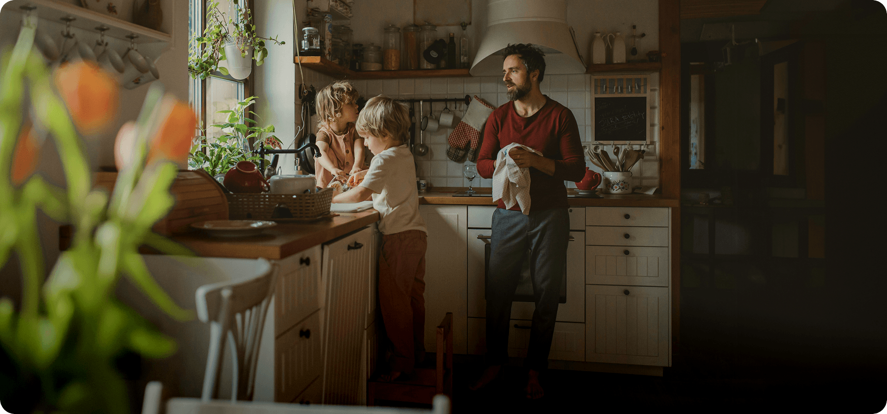 A father and two young children doing the dishes together in a warm, homely kitchen.