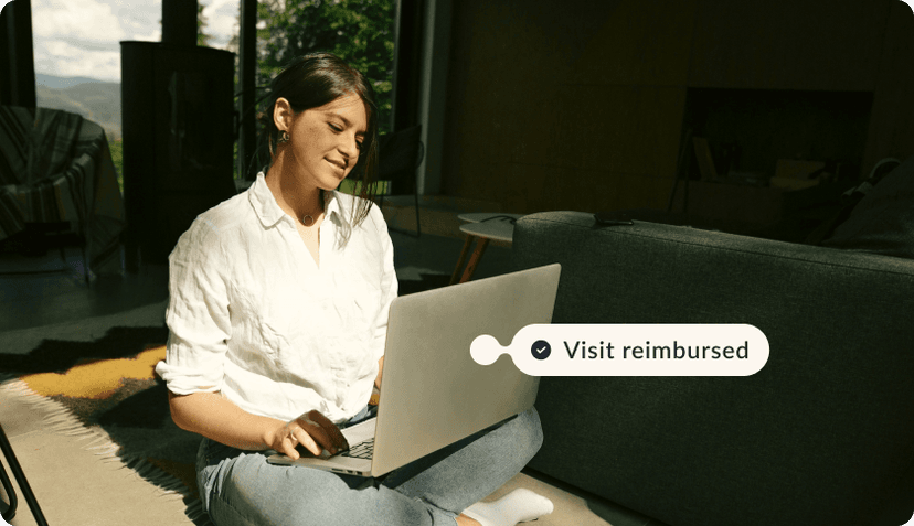 A woman looking at her laptop and smiling. The tag above the laptop reads"Visit reimbursed"