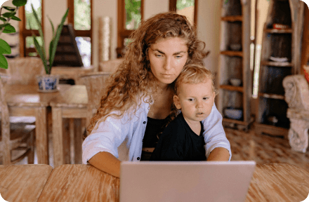 A woman sitting in front of a laptop, holding her son.